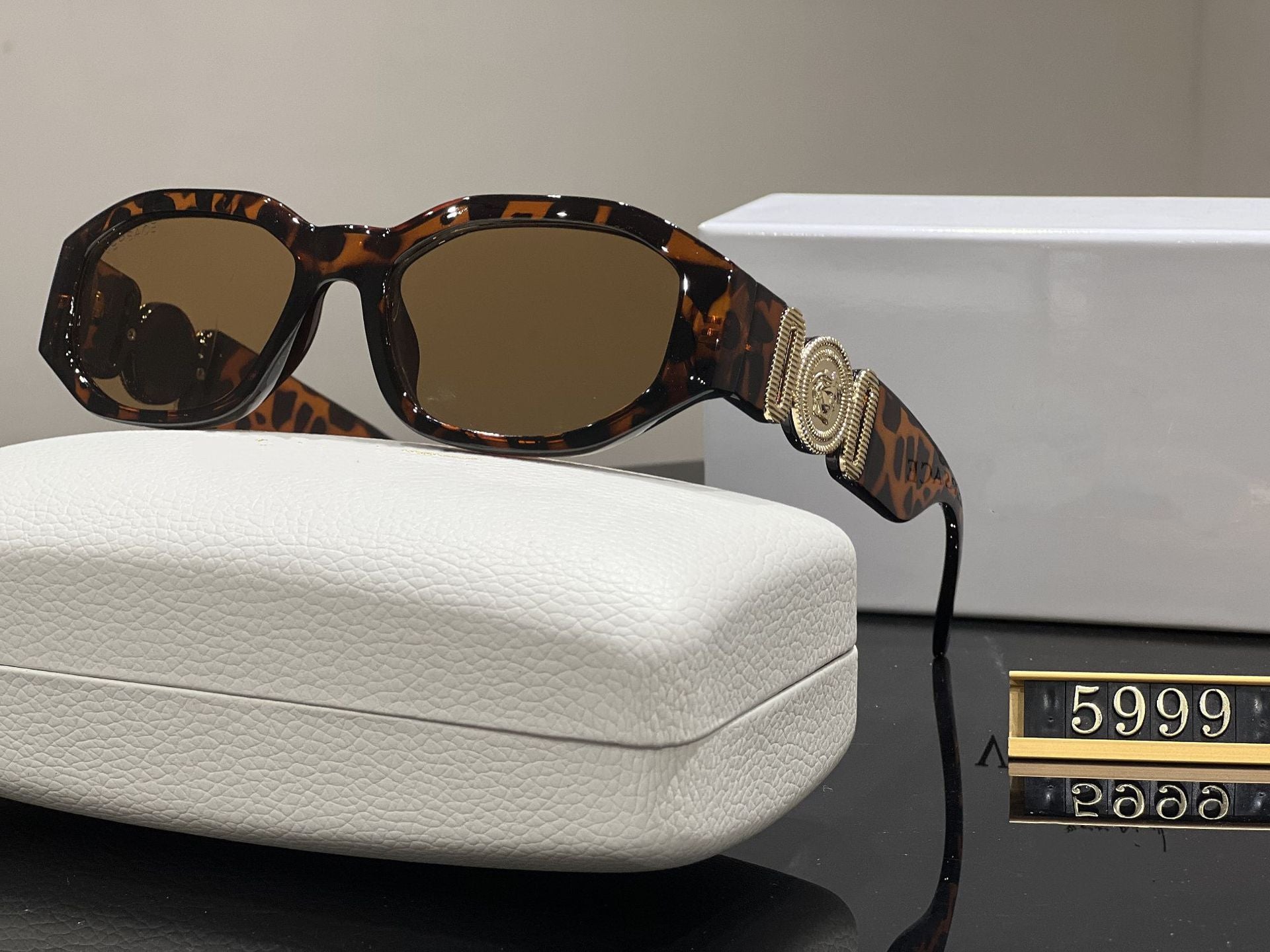 Tortoise box frame sunglasses with gold metallic temple emblem and UV protection lenses resting on a white case.