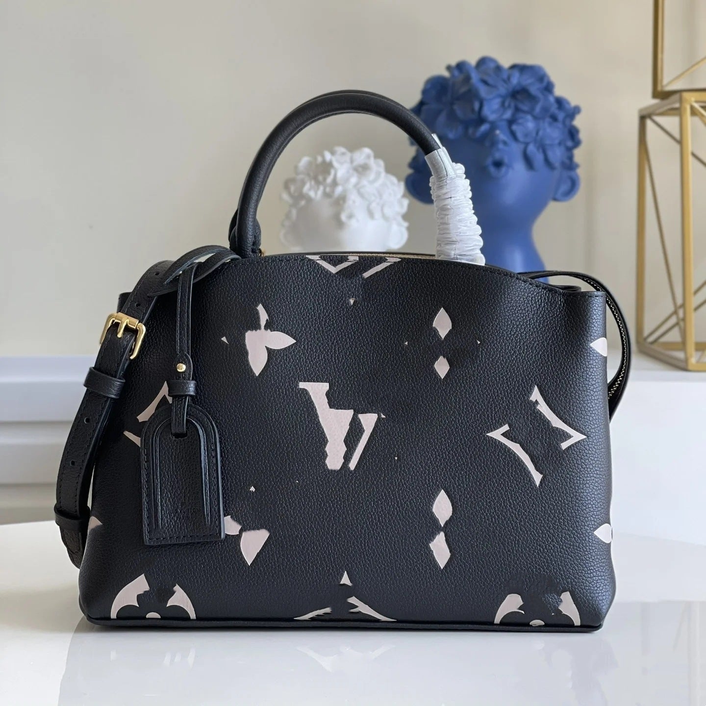 The Urban Montaigne Signature Luxe black leather handbag with white monogram pattern, gold hardware, and shoulder strap.