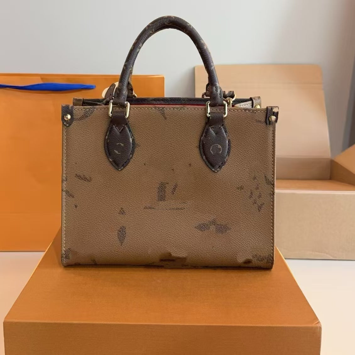 Elite Leather Shoulder Tote in beige with dark handles and gold hardware displayed on an orange box.