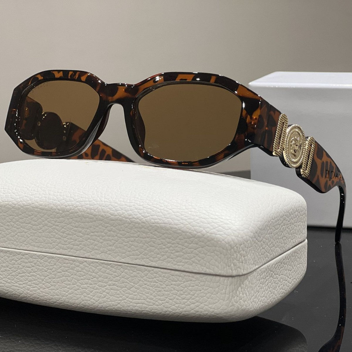 Tortoise shell box frame sunglasses with gold temple emblem and UV protection lenses resting on a white case.