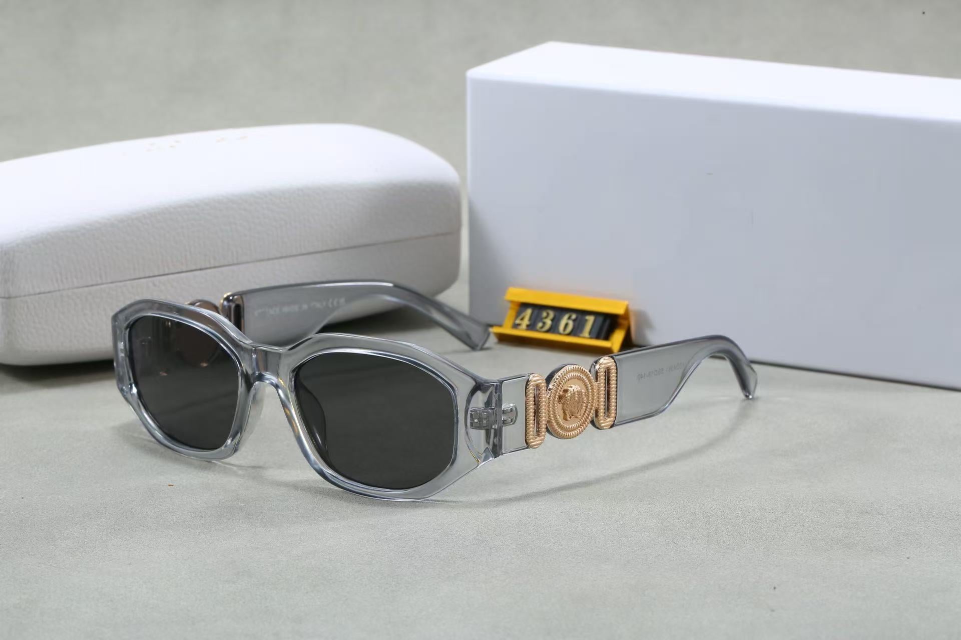 Clear box frame sunglasses with gold metallic temple emblem and UV protection lenses, shown with white case.