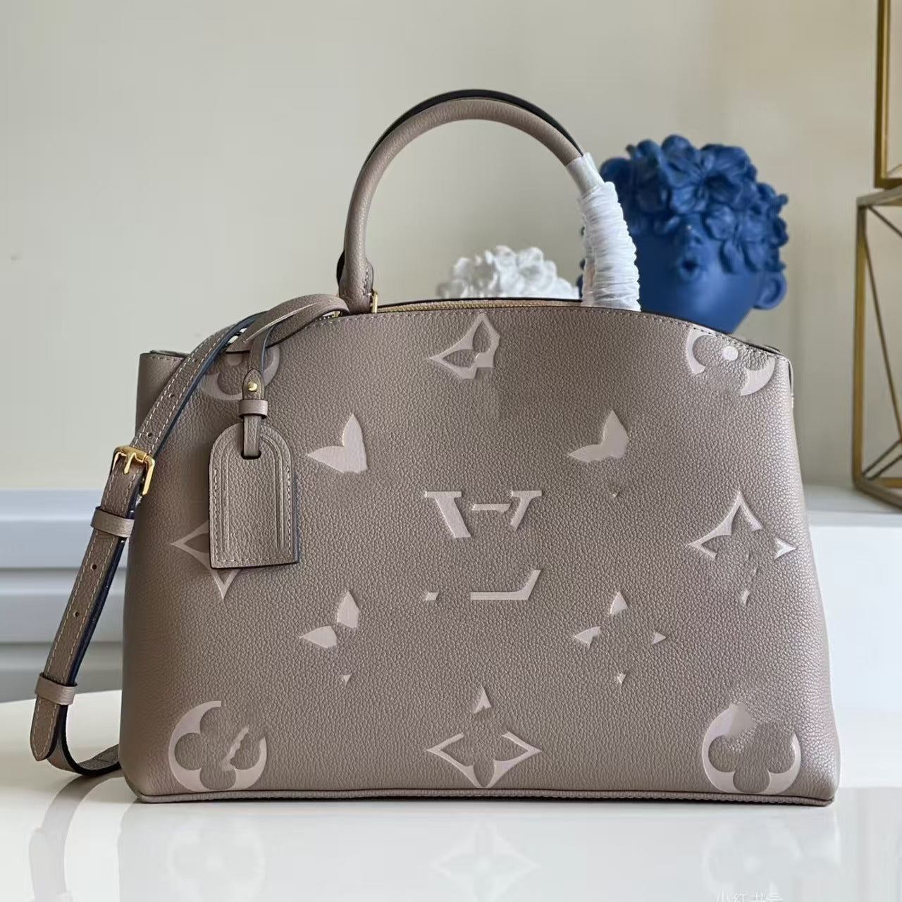 The Urban Montaigne Signature Luxe taupe handbag with glossy monogram pattern and structured silhouette on white surface.