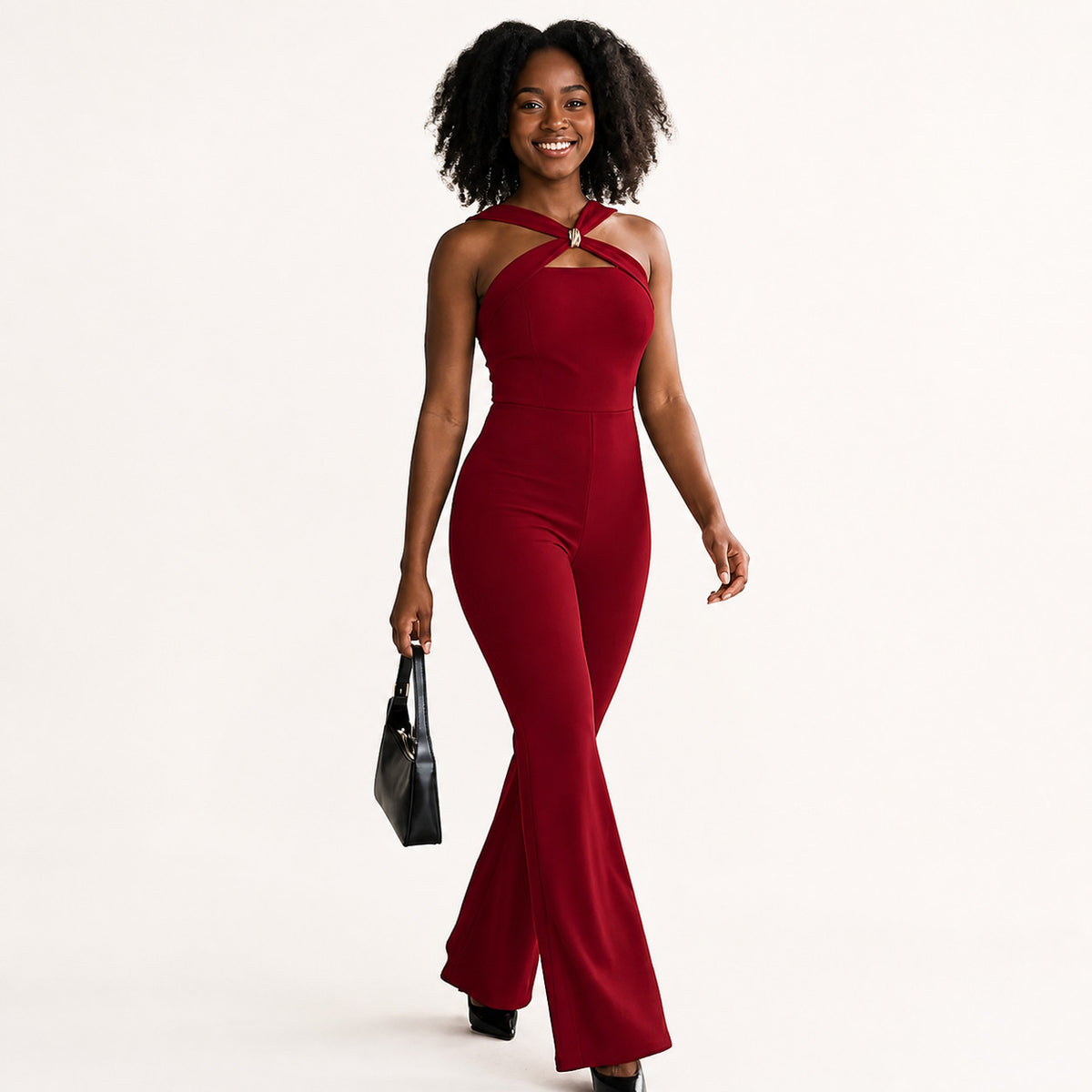 Young African American woman wearing a Luxe Buckle Flared Jumpsuit in a minimalist indoor setting, showcasing the fit and buckle detail.