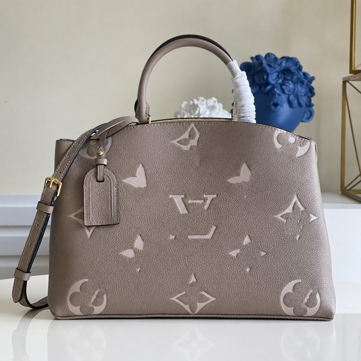 The Urban Montaigne Signature Luxe taupe handbag with glossy monogram pattern and structured silhouette on white surface.